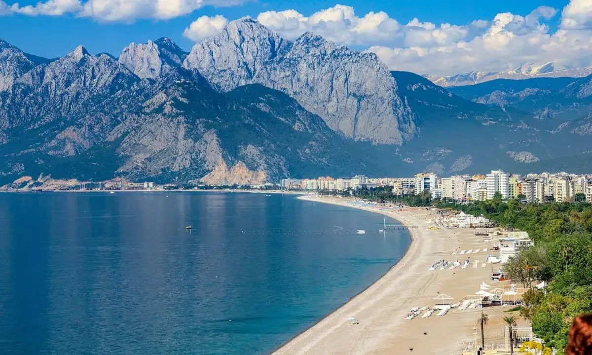 Ein malerischer antalya strand mit türkisfarbenem Wasser, weißen Bergen im Hintergrund und einer Stadtkulisse.