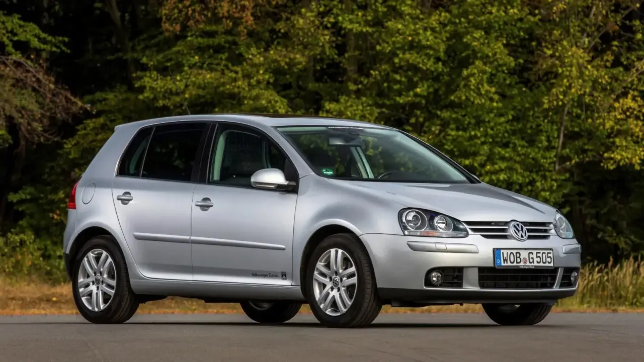 Srebrny Volkswagen Golf V stoi na drodze, otoczony zielenią drzew.