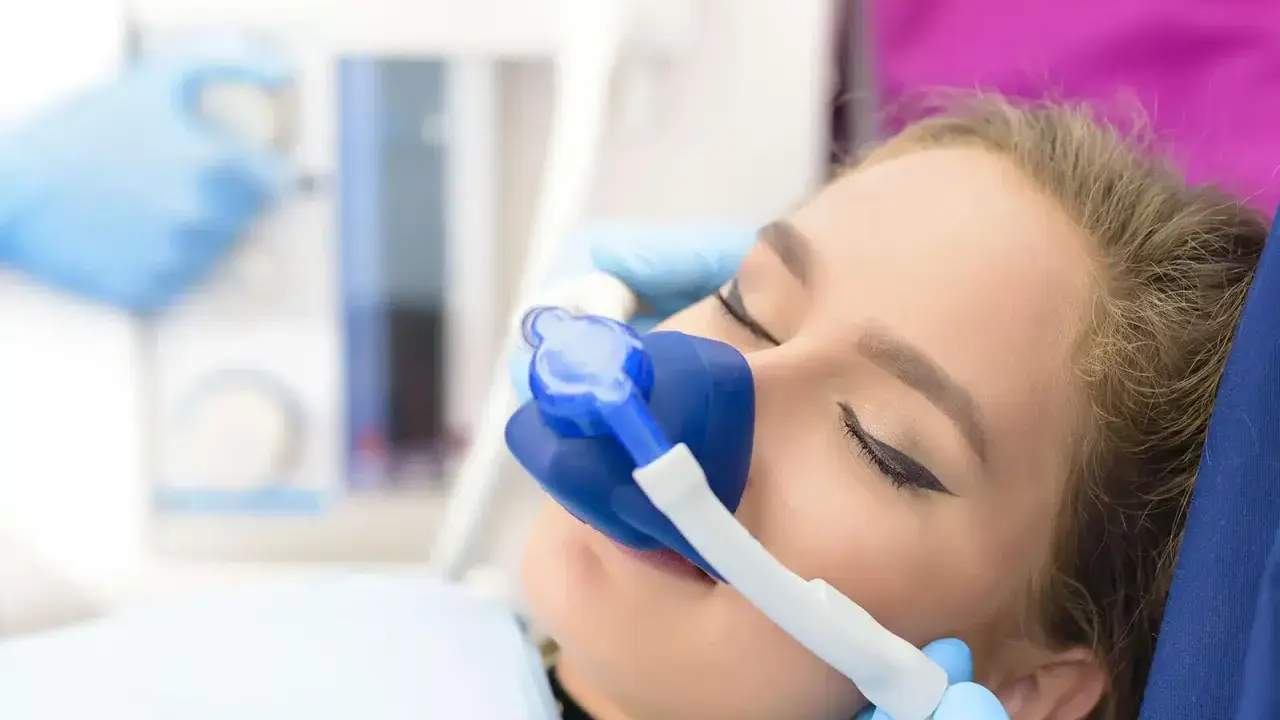 Pacjentka u dentysty z maską do podawania gazu rozweselającego. Zabieg przebiega komfortowo.