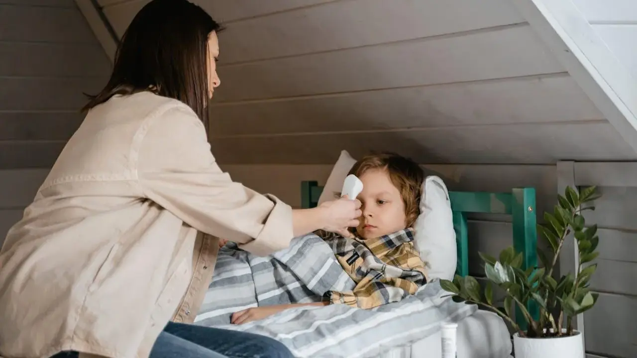 Mama mierzy gorączkę choremu dziecku, szukając domowych sposobów na zapalenie krtani u dziecka.