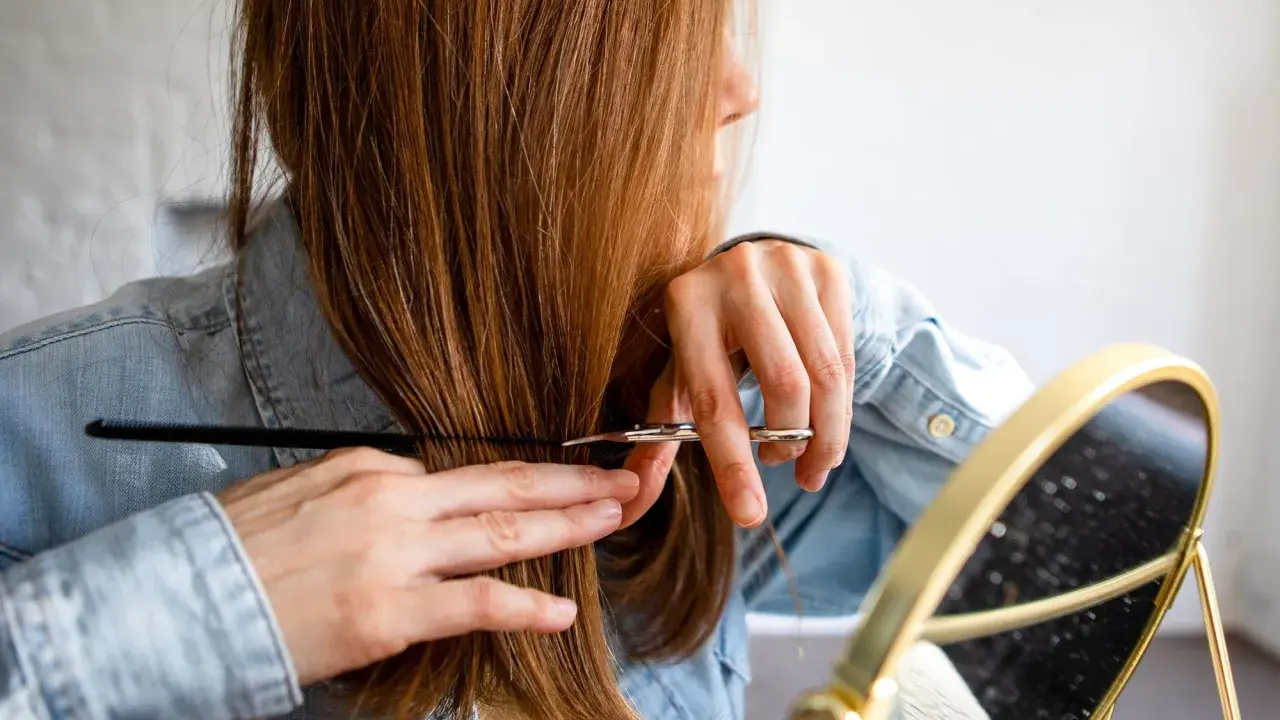 Frau mit langen, braunen Haaren, die sich im Spiegel die Haare schneidet.