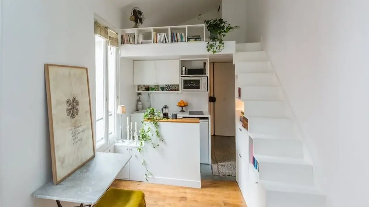 Un petit appartement optimisé avec un coin cuisine, un bureau escamotable et un escalier menant à une mezzanine. Idéal pour un **DIY rangement** créatif.