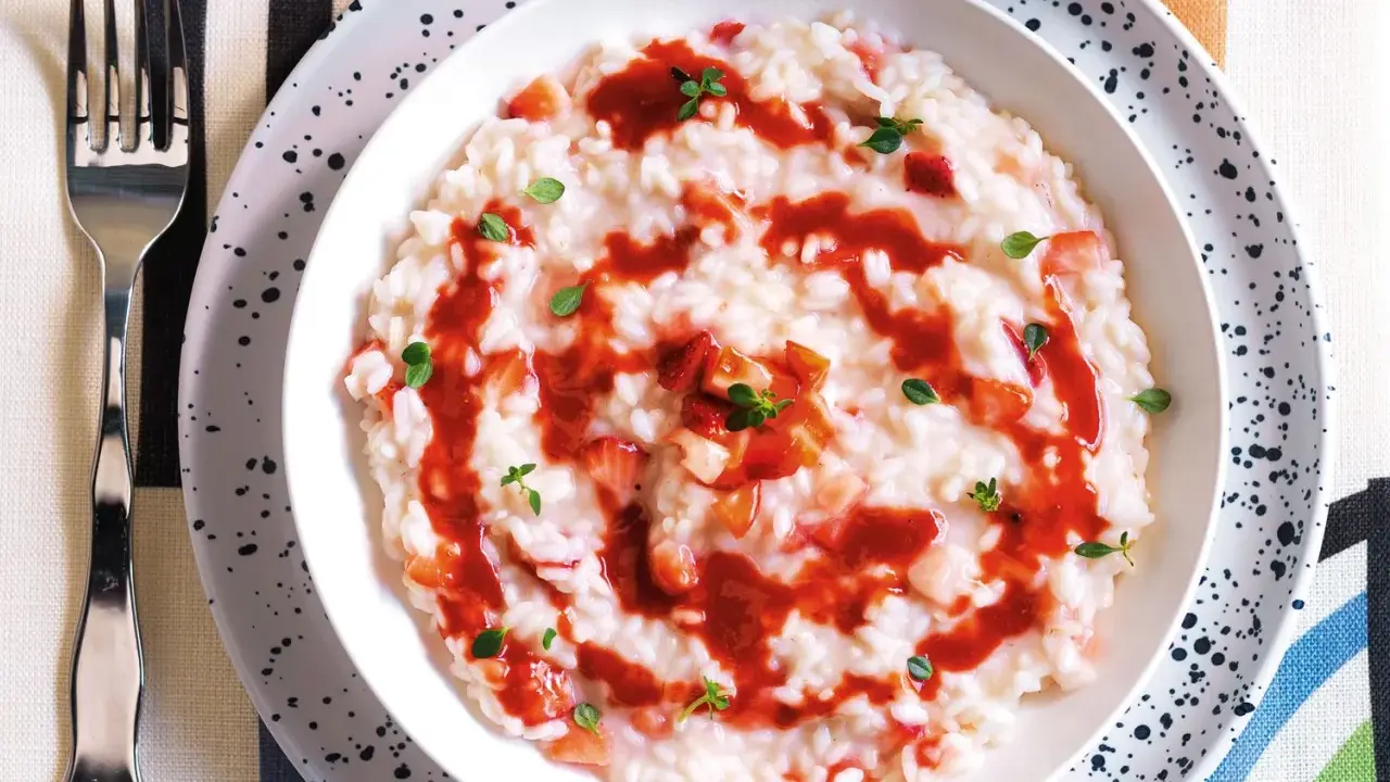 Un cremoso risotto alle fragole, guarnito con salsa di fragole e foglioline verdi, pronto per essere gustato.
