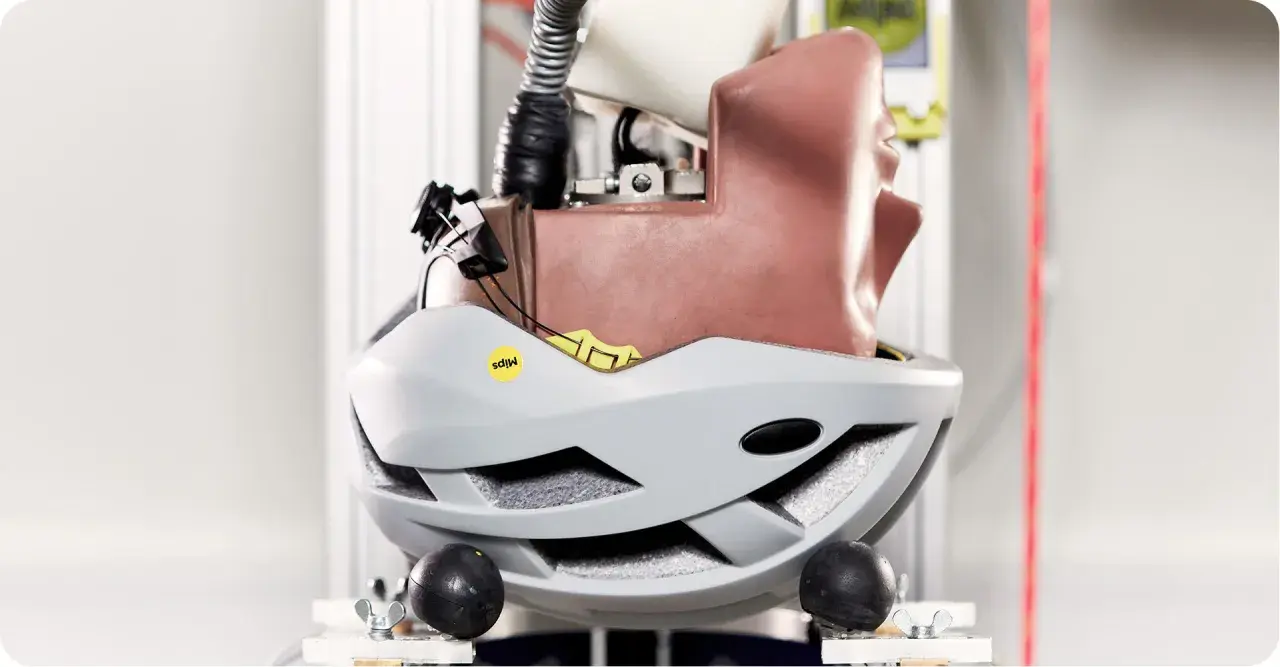 Szary kask rowerowy z technologią MIPS, zamontowany na manekinie głowy w laboratorium testowym.