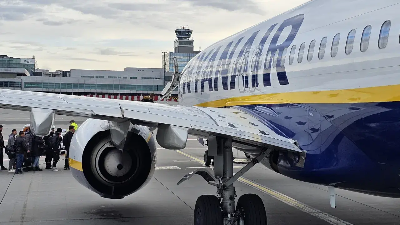 Ryanair-plan på marken med passagerare som väntar. Man undrar om man måste skriva ut boardingkort Ryanair. Flygledartorn i bakgrunden.