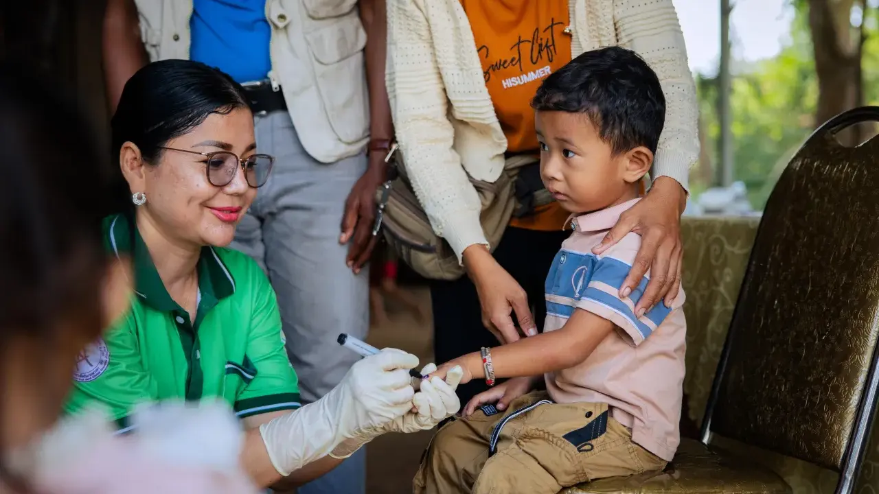 En sjukvårdare med handskar markerar ett barns finger efter vaccination i Kambodja.