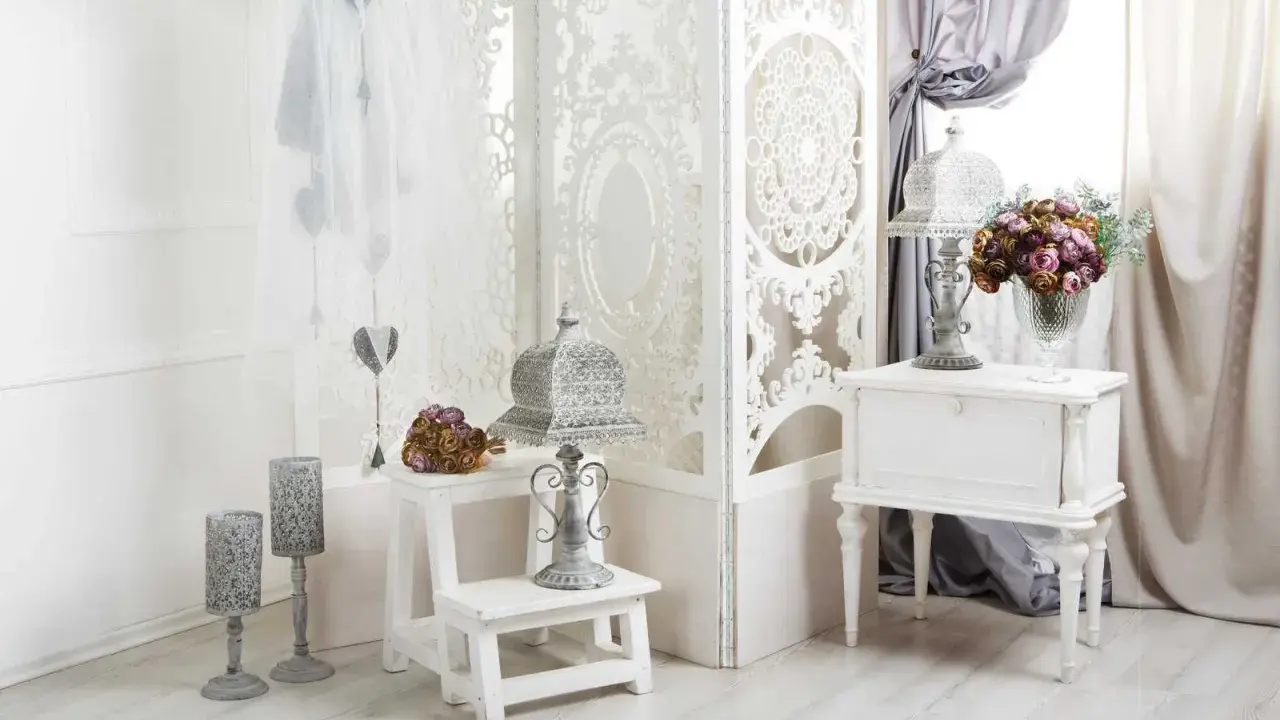 Delikatny salon w stylu shabby chic. Białe meble, ażurowa parawan, świeże kwiaty i ozdobne latarenki tworzą romantyczny nastrój.