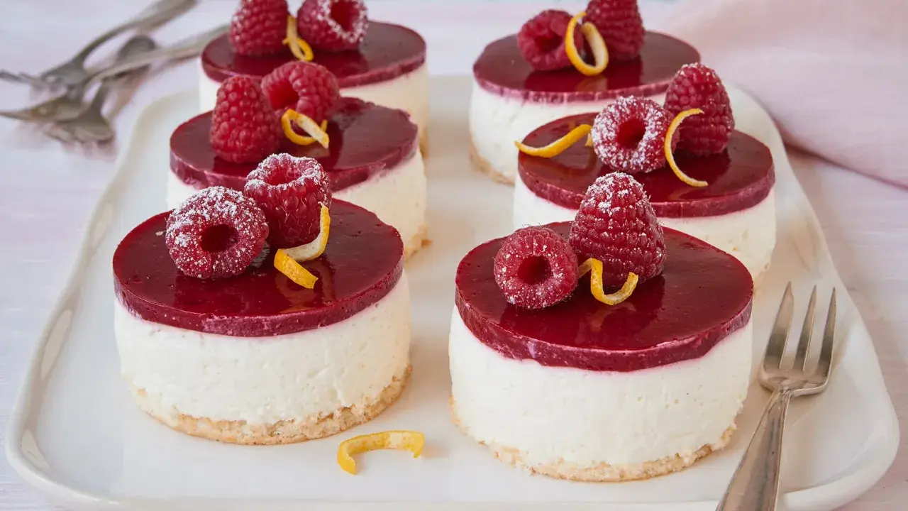 Sechs kleine Kuchen mit Himbeeren und Zitronenzesten auf einem weißen Teller.
