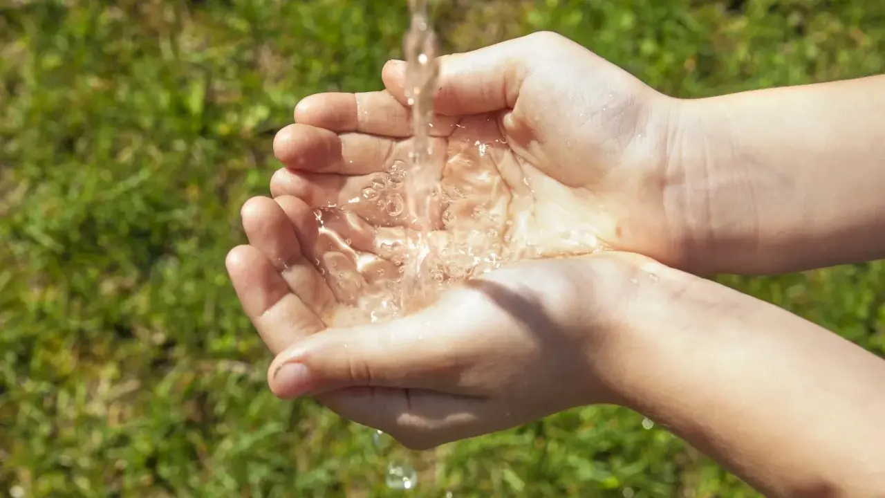 Mains d'enfant recevant un filet d'eau, une façon simple de rendre l'eau moins calcaire pour un usage quotidien.