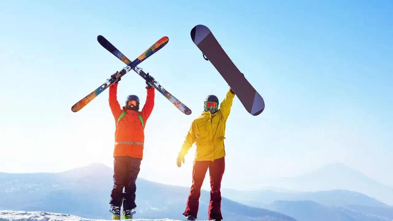 Dwóch narciarzy na szczycie góry, jeden z nartami, drugi z deską snowboardową, cieszy się słońcem i widokiem.