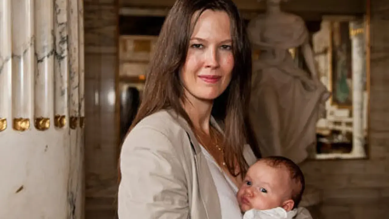 Elin Klinga med sitt barn. En vacker mamma med sitt nyfödda barn i famnen, omgivna av klassisk arkitektur.