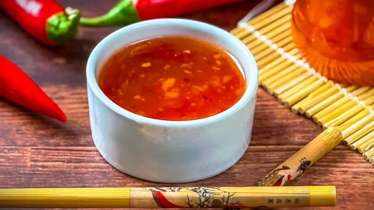 Schüssel mit leuchtend roter Sweet Chilli Sauce, daneben rote Chilis und Stäbchen. Perfekt für dein Sweet Chilli Sauce Rezept!