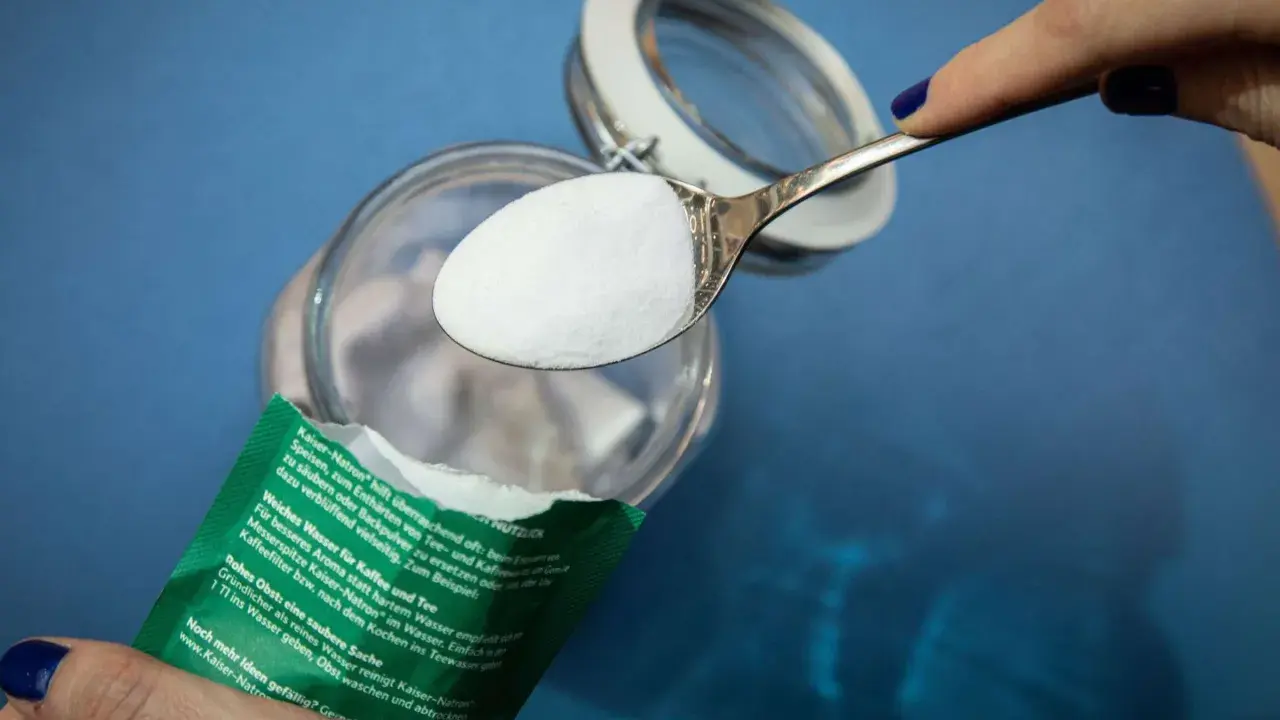 Ein Löffel Natron wird über ein Glas gehalten. Ein natürliches Hausmittel zur Geruchsneutralisierung und Reinigung.