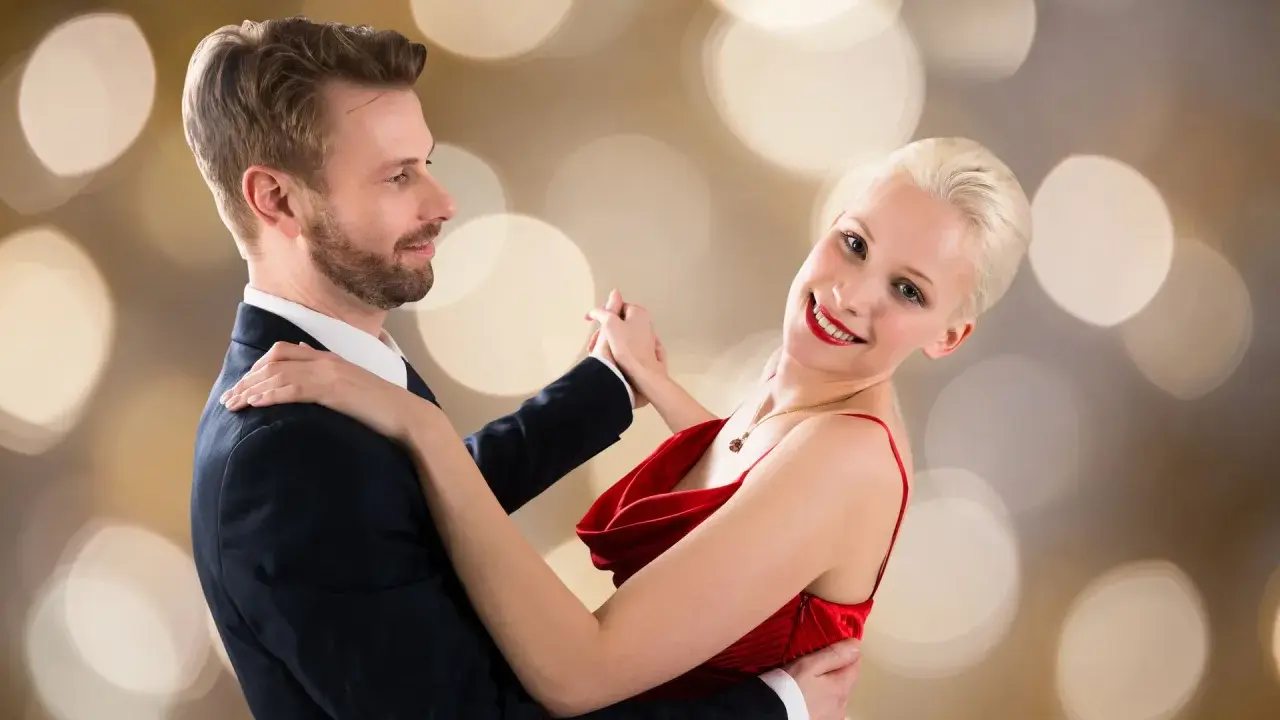 Para tańczy walca angielskiego na tle złotych bokeh. Ona w czerwonej sukni, on w garniturze.