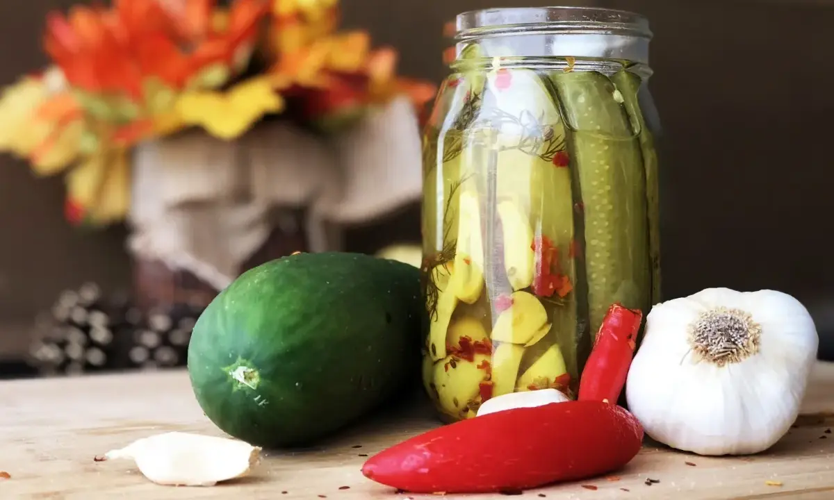 Słoik z ogórkami z chili w plastrach, obok świeży ogórek, czosnek i papryczka chili.