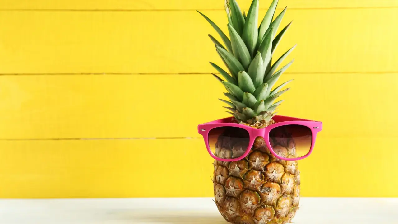 Ananas w okularach przeciwsłonecznych na żółtym tle. Czy wiesz, jaki ananas indeks glikemiczny ma dla Twojej diety?