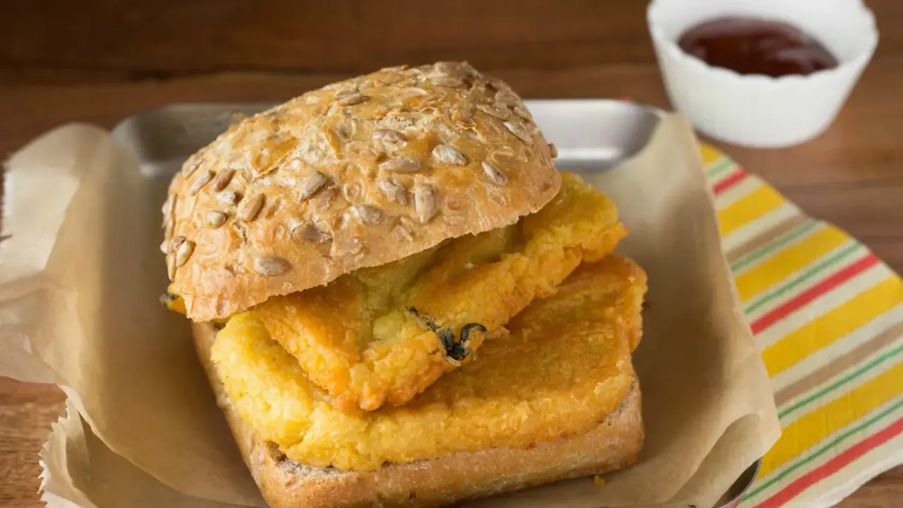 Panino con pane e panelle fritte, un classico street food siciliano, servito su un vassoio con carta da forno e una ciotolina di salsa.