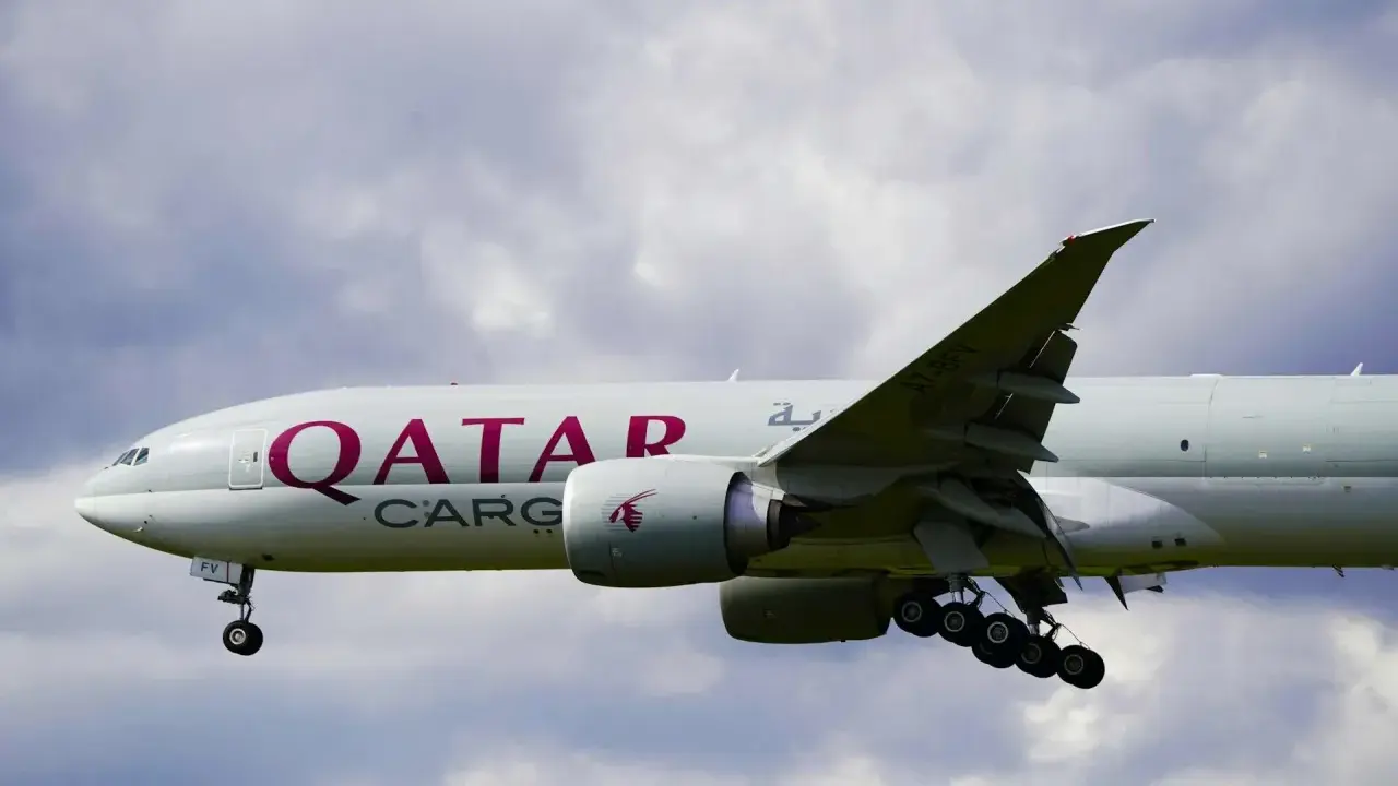 Samolot Qatar Airways Cargo z wysuniętym podwoziem, gotowy do lądowania. W tle chmury.