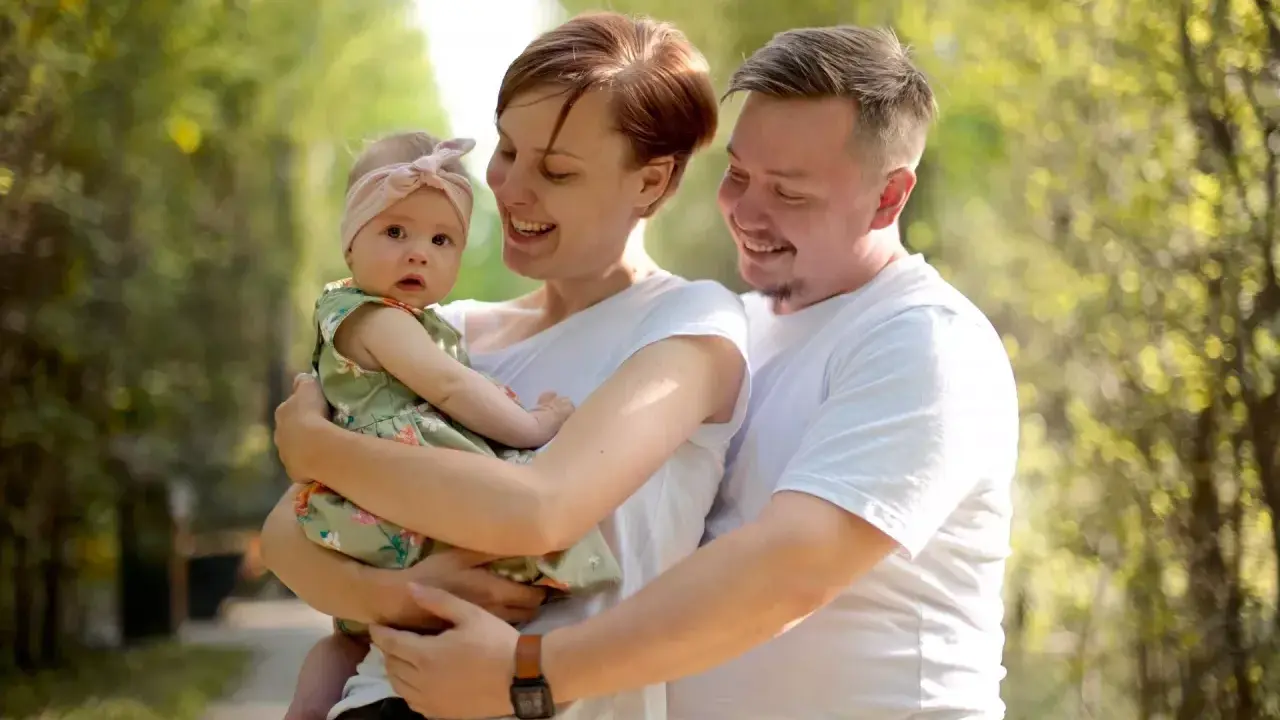 Szczęśliwa rodzina z córeczką w letnim parku. Mama tuli dziecko, tata obejmuje ich. Idealne babciowe warunki na spacer.