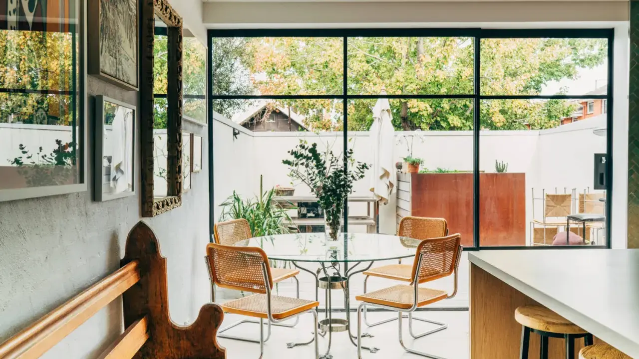 Sedie in paglia e metallo, ispirate a Marcel Breuer, attorno a un tavolo di vetro in una luminosa sala da pranzo con vista sul giardino.