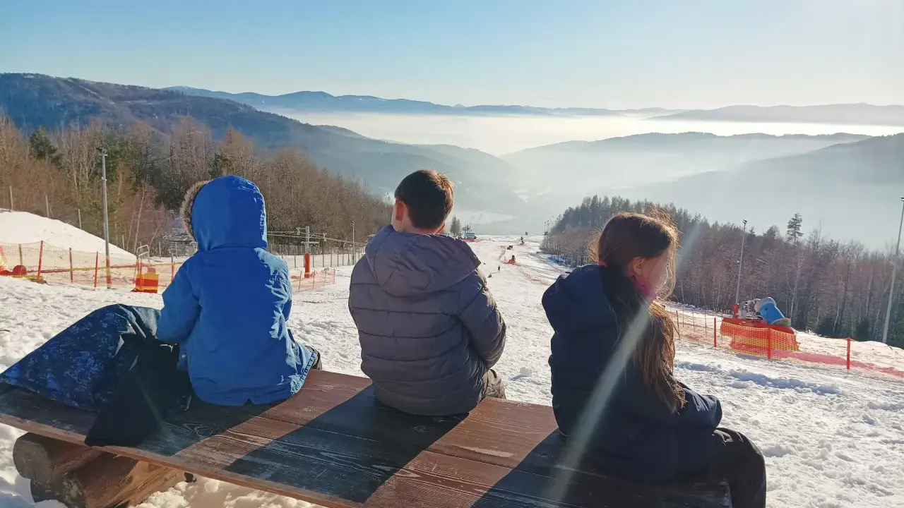Dzieci siedzą na ławce, podziwiając widok na góra żar i dolinę spowitą mgłą.