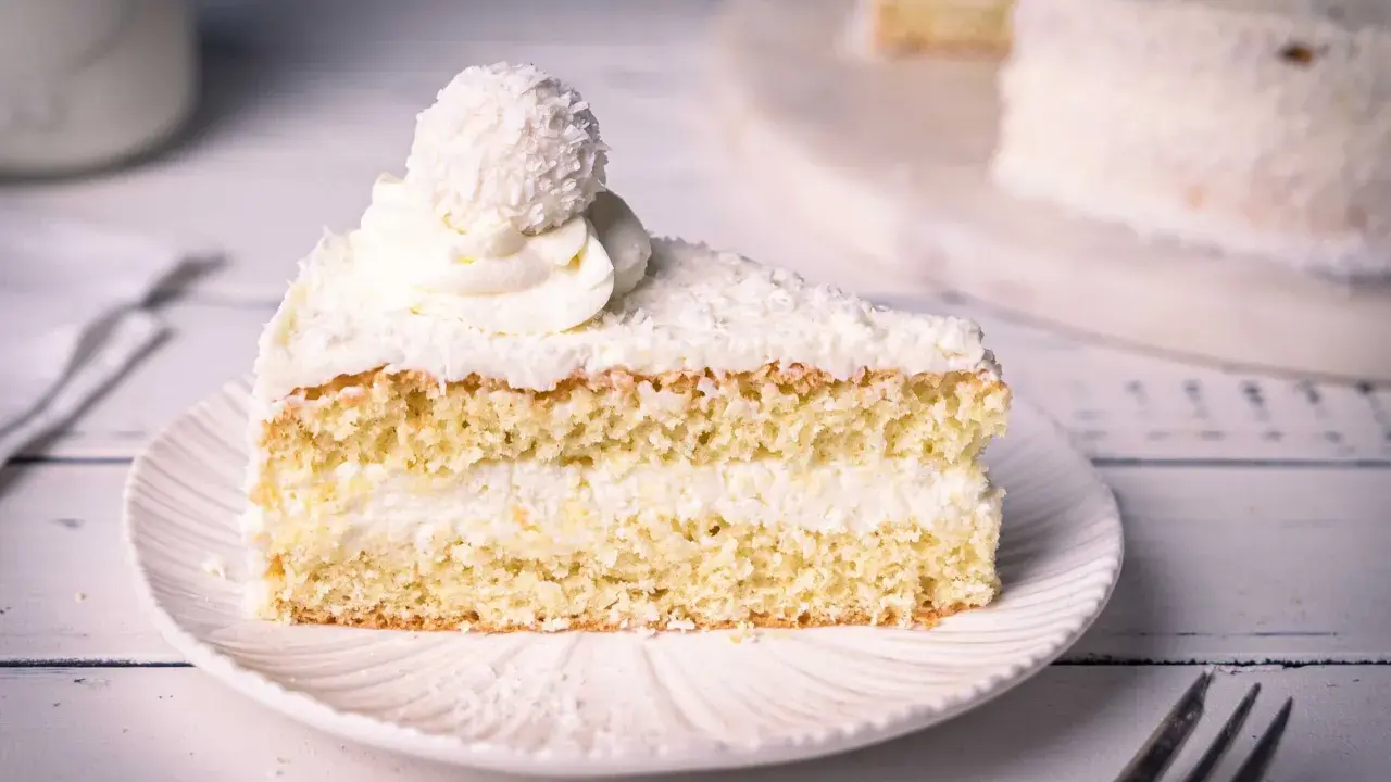Ein saftiges Stück Raffaello Torte mit Kokosraspeln und Sahne, gekrönt von einer Raffaello-Kugel.