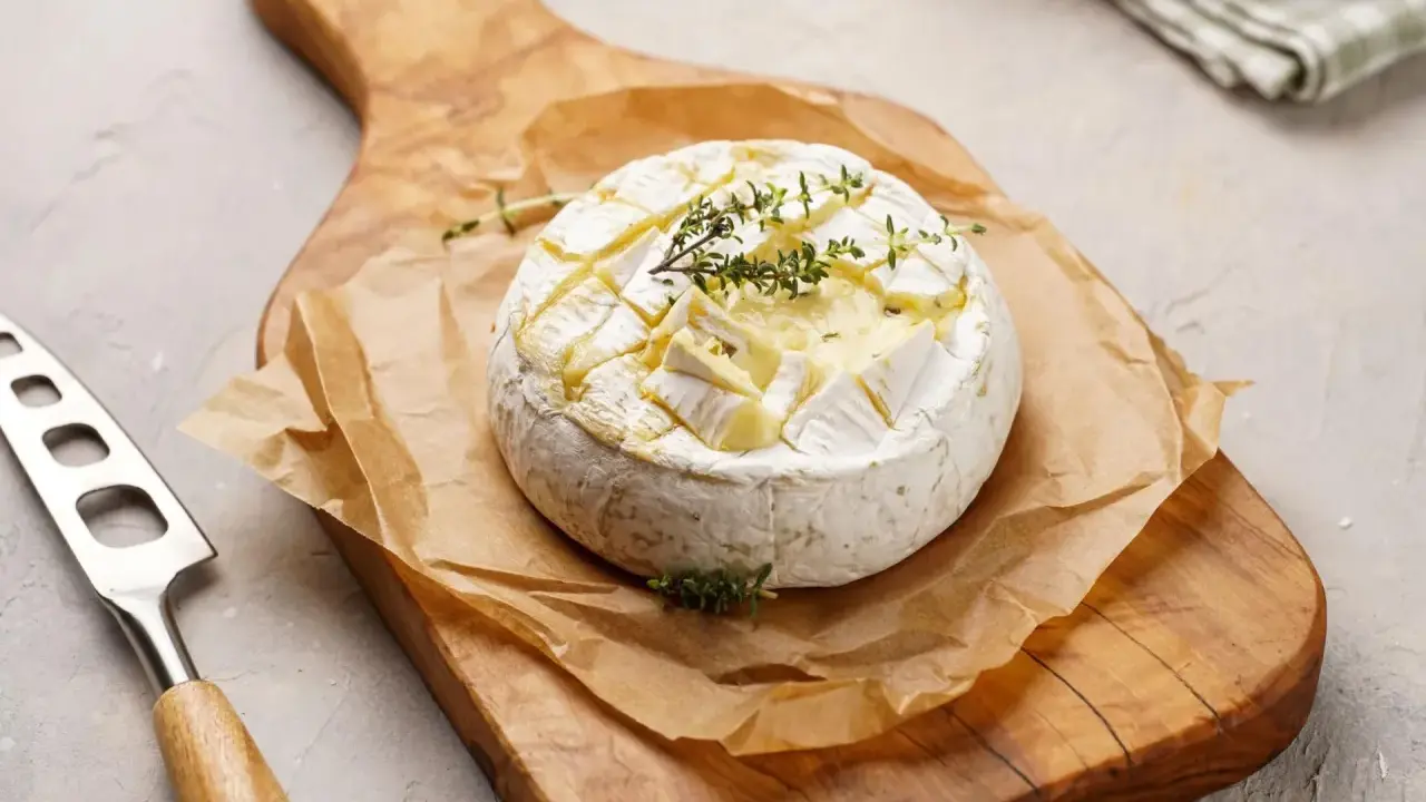 Pyszny camembert z grilla, zapieczony z ziołami, na drewnianej desce. Idealny do maczania.