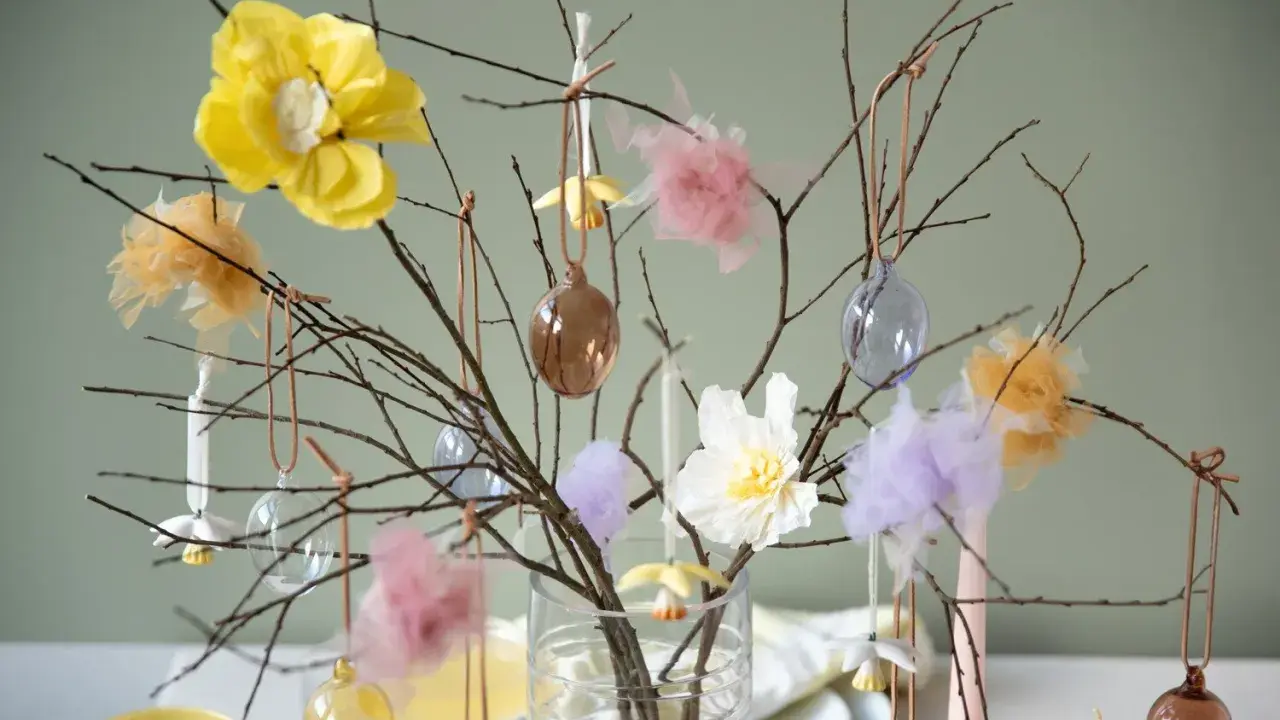 Vacker påskris inspiration med grenar dekorerade med glaskulor, tygblommor och fluffiga dekorationer i pastellfärger.