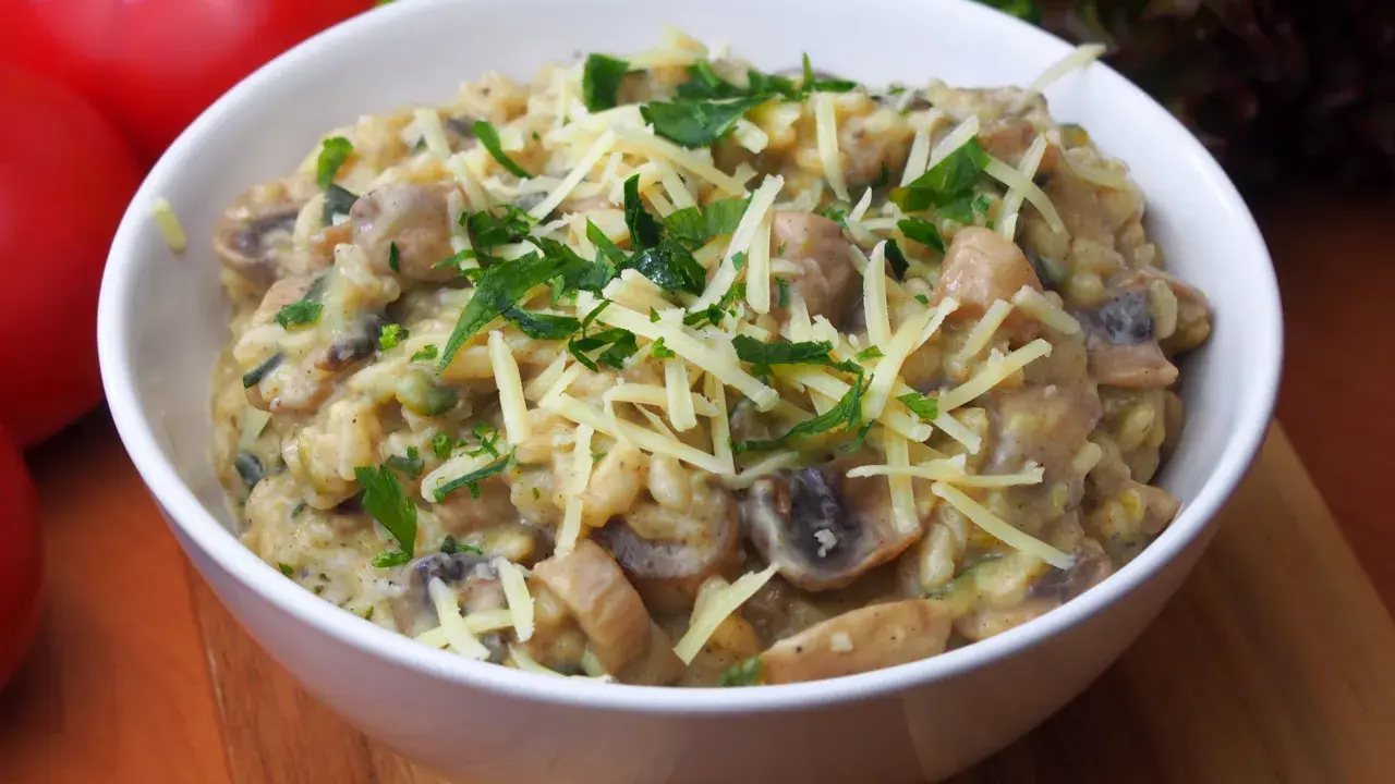 Pyszne risotto z pieczarkami, posypane startym serem i świeżą natką pietruszki, czeka w białej miseczce.