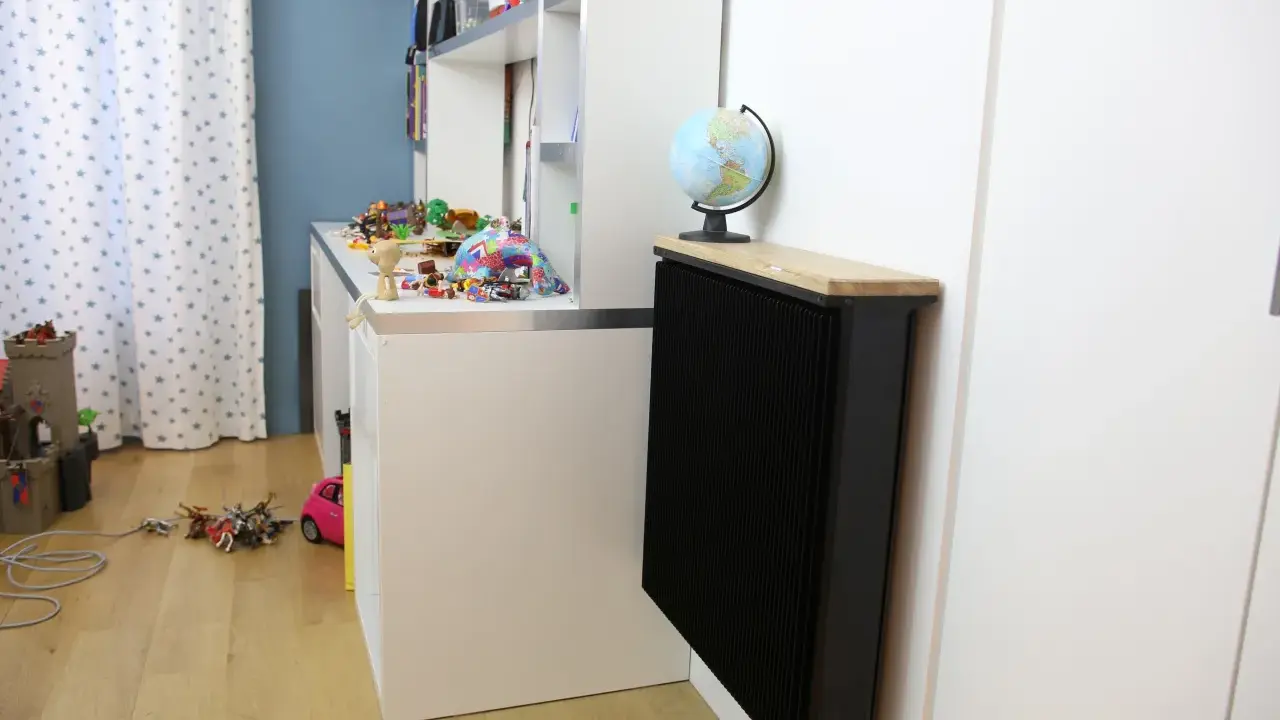 Un radiateur Qarnot particulier noir, surmonté d'un plateau en bois et d'un globe, réchauffe la chambre d'enfant remplie de jouets.