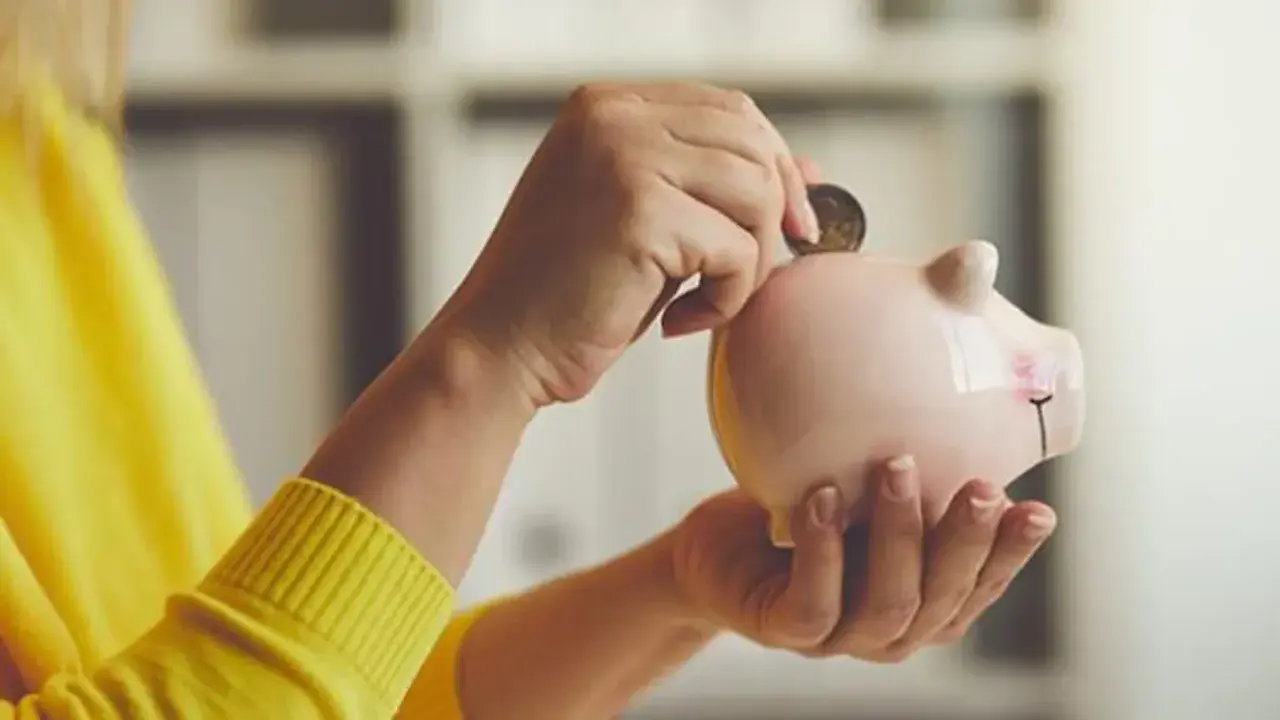 Manos introducen una moneda en una hucha rosa, simbolizando el ahorro para recuperar plan de pensiones nueva ley.