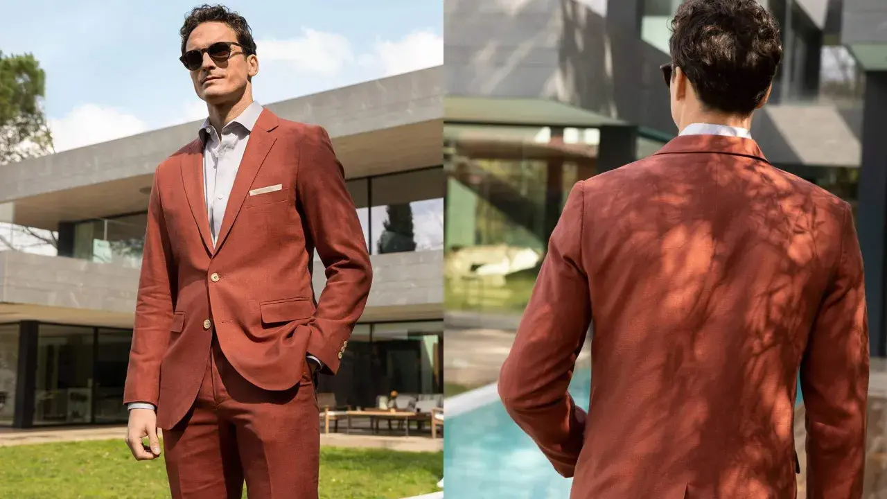 Man in a rust-colored suit, perfect semi formal attire for a wedding. He wears sunglasses and a light shirt, looking dapper outdoors.
