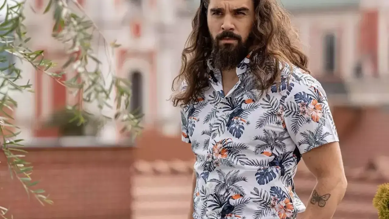 Mężczyzna z długimi włosami w hawajskiej koszuli na t-shirt, z motywem liści i ptaków.