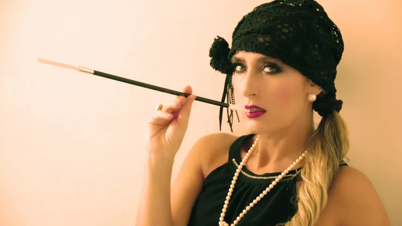 Glamurosa mujer con maquillaje de los años 20, sombrero negro y boquilla.