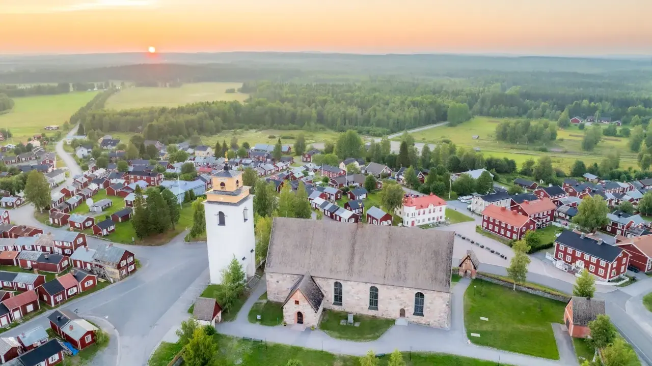 Gammelstad Luleå: en kyrka och ett kluster av röda trähus under en solnedgång.