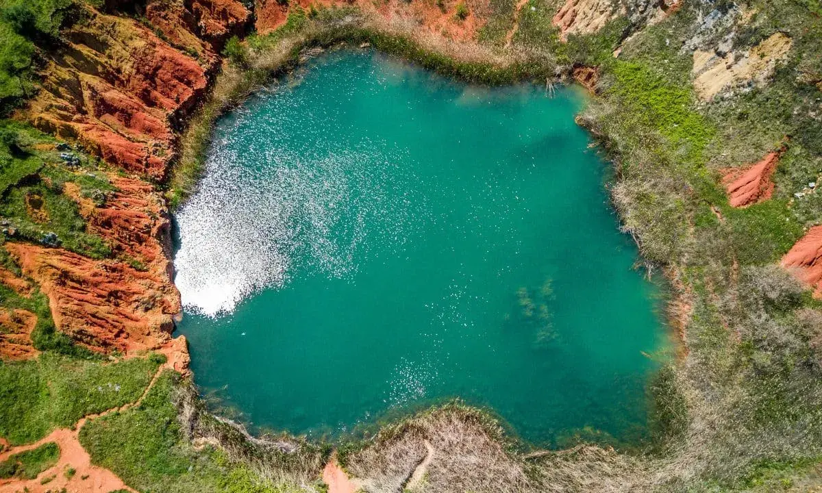 Lago turchese circondato da rocce rosse e vegetazione rigogliosa, un paesaggio suggestivo che ricorda le cave di bauxite.