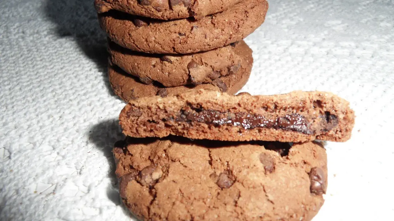 Gros plan sur une pile de biscuits au chocolat, dont un est coupé en deux révélant un cœur coulant de Nutella. Une recette de biscuit Nutella parfaite pour les gourmands.