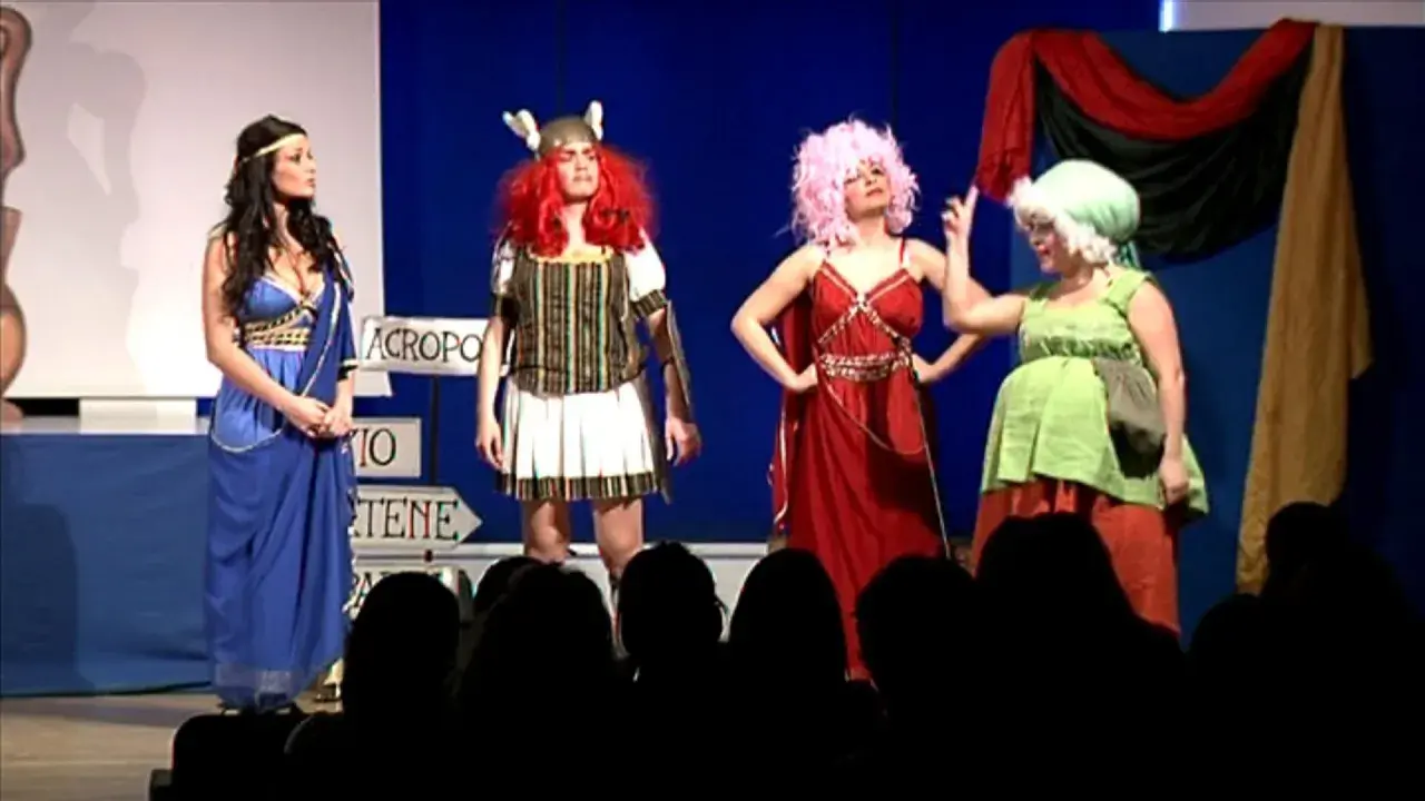 Attrici in costume su un palco, forse per la lisistrata trama. Una in blu, una guerriera, una con capelli rosa e una in verde.