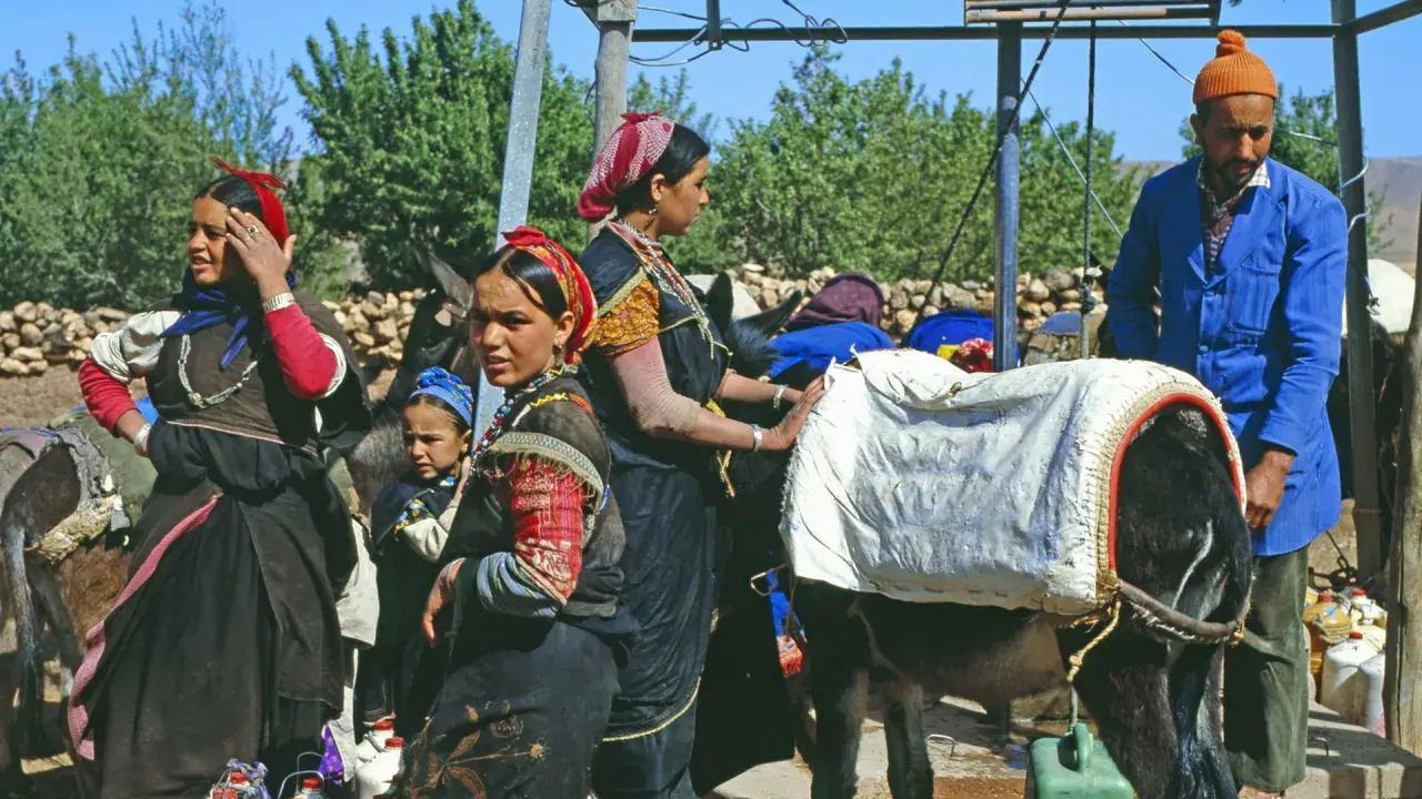 Berber Marokko Frauen mit Eseln, beladen mit Säcken. Ein Mann in blauer Jacke steht daneben.