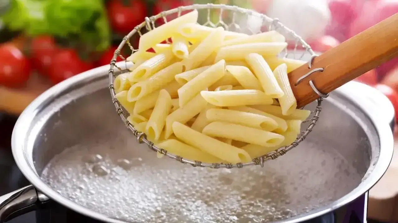 Gotowanie penne do pysznych dań z makaronem. W tle pomidory i sałata.