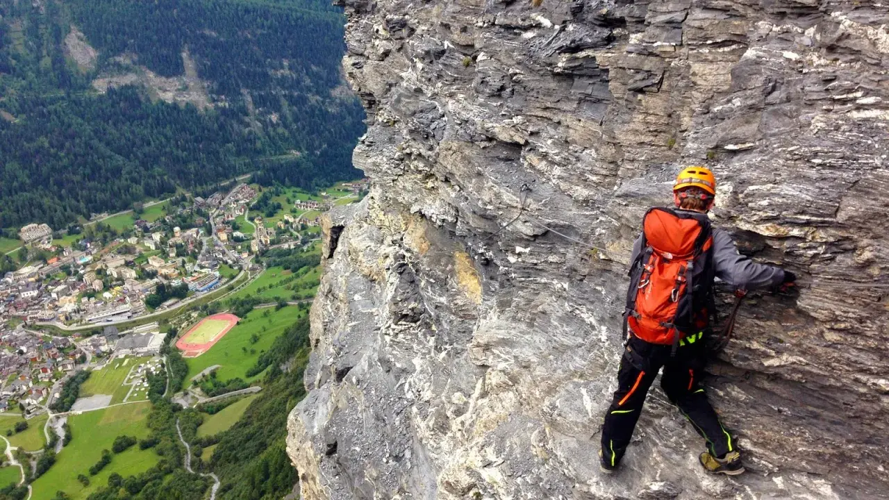 Wspinaczka via ferrata w Szwajcarii. Widok na dolinę i miasteczko z perspektywy skalnej ściany.
