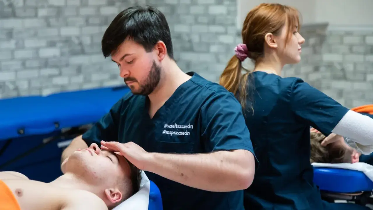 Młodzi terapeuci podczas zajęć praktycznych z fizjoterapii w Poznaniu. Jeden z nich wykonuje masaż głowy pacjentowi.