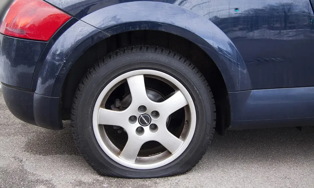 Ruota posteriore di un'auto blu con evidente perdita pressione pneumatici. Il pneumatico è sgonfio e appoggiato a terra.