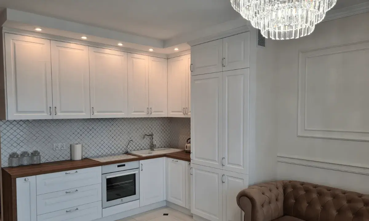 Elegancka kuchnia w stylu angielskim z białymi frontami, drewnianym blatem i kryształowym żyrandolem.