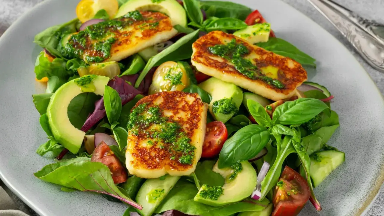 Pyszna sałatka z halloumi, awokado, pomidorkami i świeżymi ziołami, polana zielonym dressingiem.