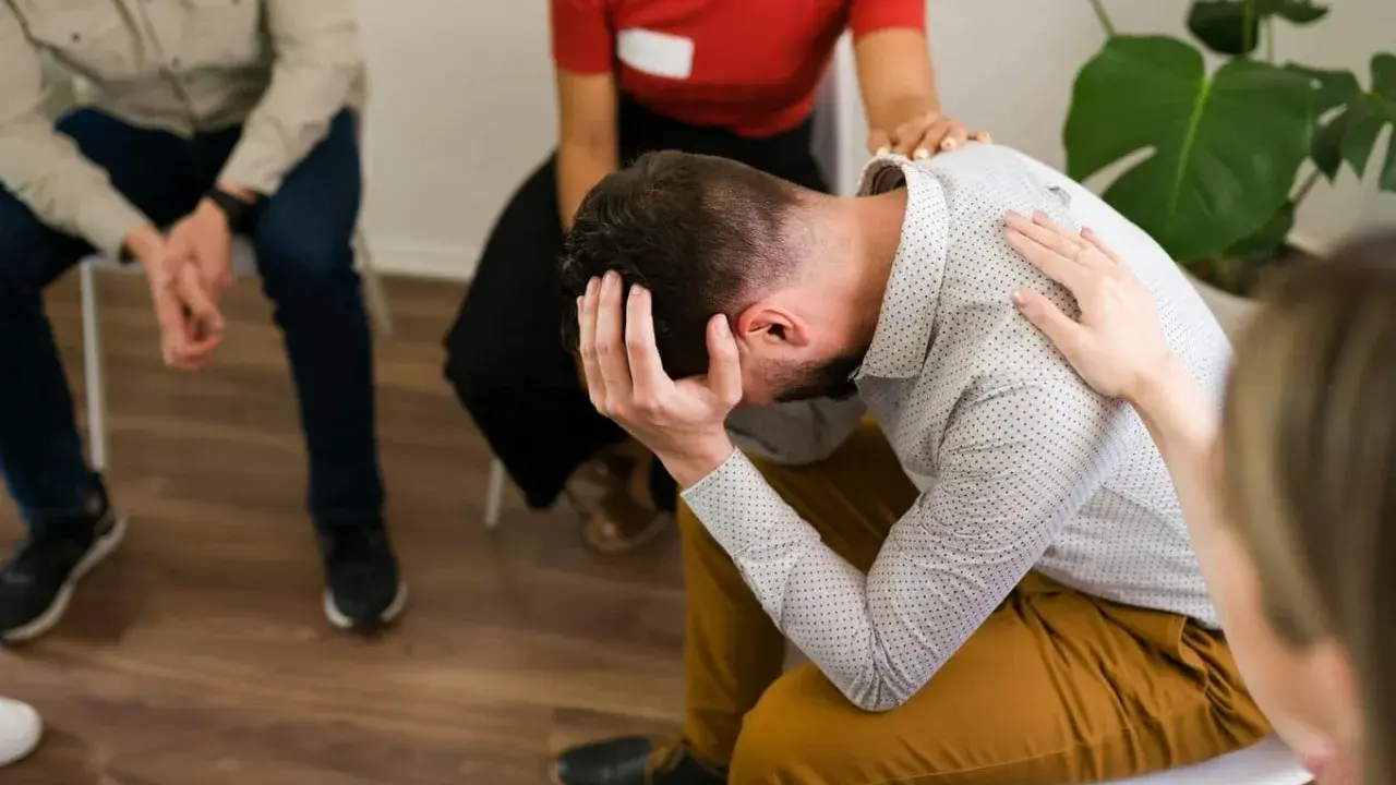 Grupa wsparcia dla osób walczących z nałogiem. Mężczyzna w centrum trzyma się za głowę, czując się przytłoczony.