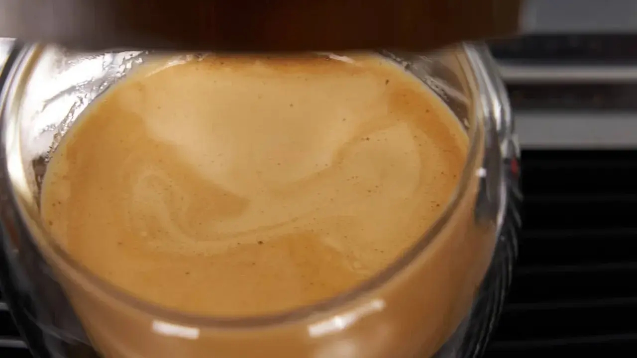Ein Glas mit cremigem Kaffee, das ist cafe crema mit milch. Die goldbraune Crema wirbelt sanft.
