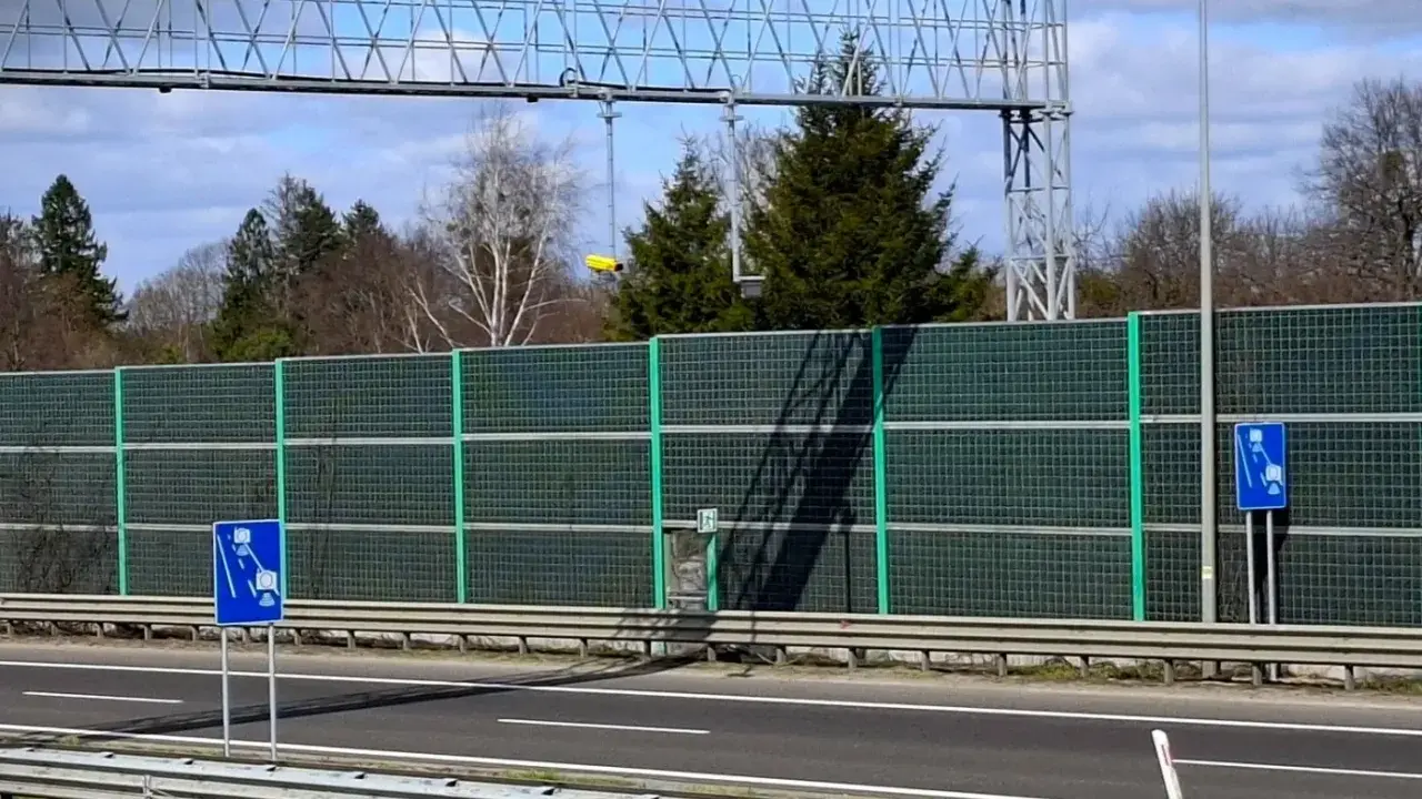 Znak informujący o odcinkowym pomiarze prędkości S3. Za ekranami akustycznymi widać drzewa i niebo.