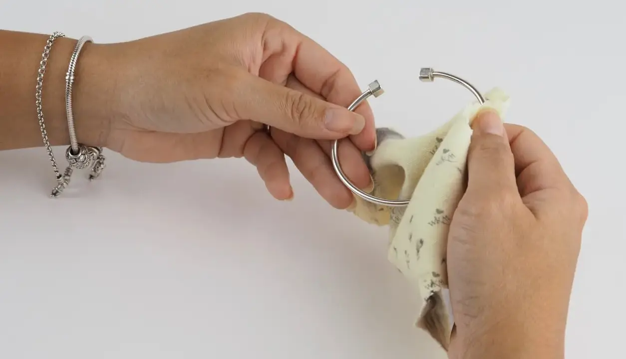 Manos puliendo un brazalete de plata con un paño. Aprende como limpiar cadena de plata y mantener tus joyas brillantes.