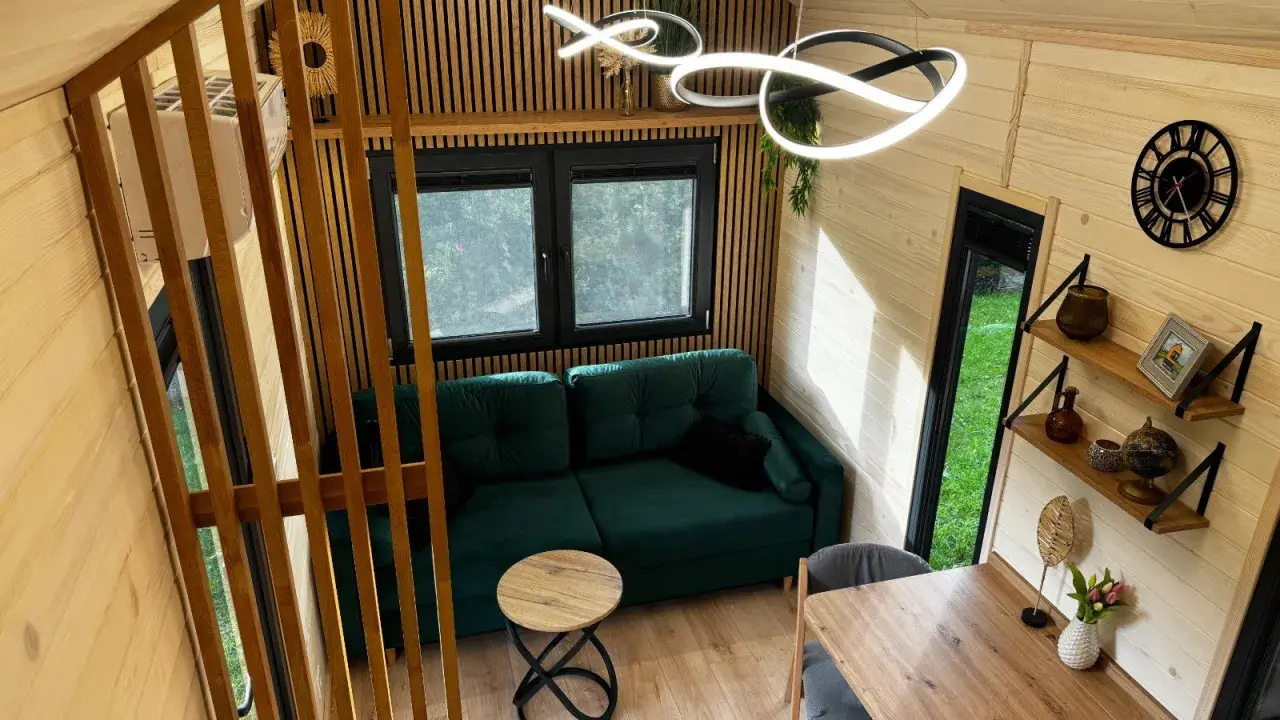 Przytulne wnętrze tiny house Polska: zielona kanapa, drewniane meble i nowoczesne oświetlenie. Idealne miejsce na relaks.